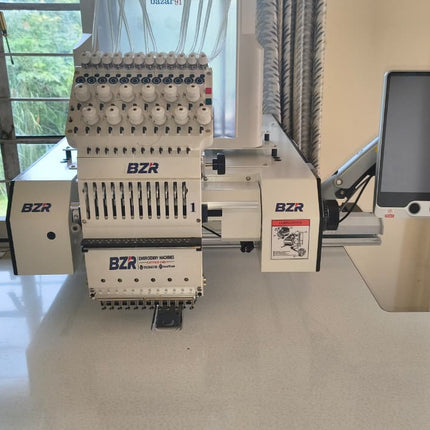 A BZR industrial embroidery machine with a multi-needle head and an attached touchscreen display, set on a white table in front of a window.